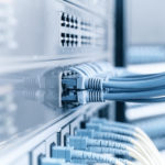 Darstellung einer IT-Infrastruktur: Nahaufnahme von mehreren blauen Ethernet-Kabeln, die in Netzwerk-Switches eingesteckt sind. Die Kabel verlaufen geordnet in verschiedene Ports, während das Bild eine klare, technisch saubere Umgebung vermittelt.