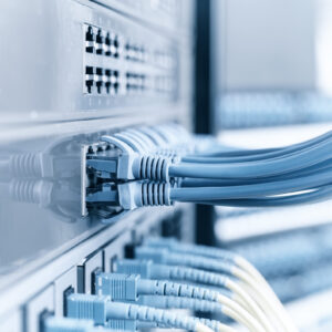 Darstellung einer IT-Infrastruktur: Nahaufnahme von mehreren blauen Ethernet-Kabeln, die in Netzwerk-Switches eingesteckt sind. Die Kabel verlaufen geordnet in verschiedene Ports, während das Bild eine klare, technisch saubere Umgebung vermittelt.