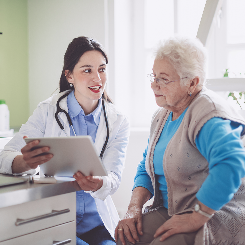 Eine freundliche Ärztin aus der regionalen Krankenversorgung berät eine ältere Patientin mit Hilfe digitaler Gesundheitsinformationen auf einem Tablet.