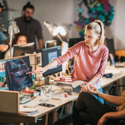 Zwei junge Data Scientists einer Nachwuchsgruppe sitzen in einem Büro an einem Tisch und diskutieren am Bildschirm einen Code.