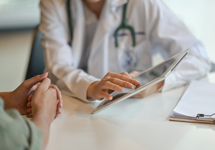 Eine Ärztin aus der regionalen Gesundheitsversorgung zeigt einer Patientin auf einem Tablet ihre medizinischen Daten.