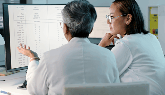 © istockphoto.com/Kobus Louw 1483251775 Zwei Wissenschaftlerinnen oder Ärztinnen in weißen Kitteln sitzen vor einem Computerbildschirm und analysieren medizinische Daten